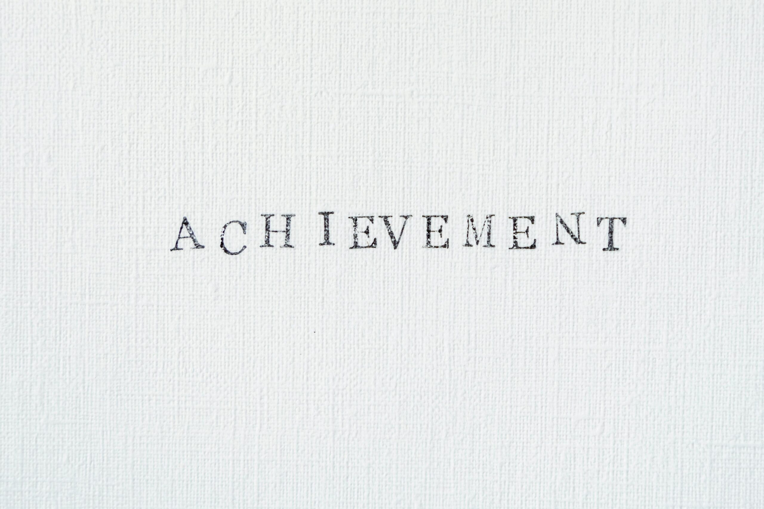 Close-up of the word 'achievement' on a textured white background, perfect for motivation themes.